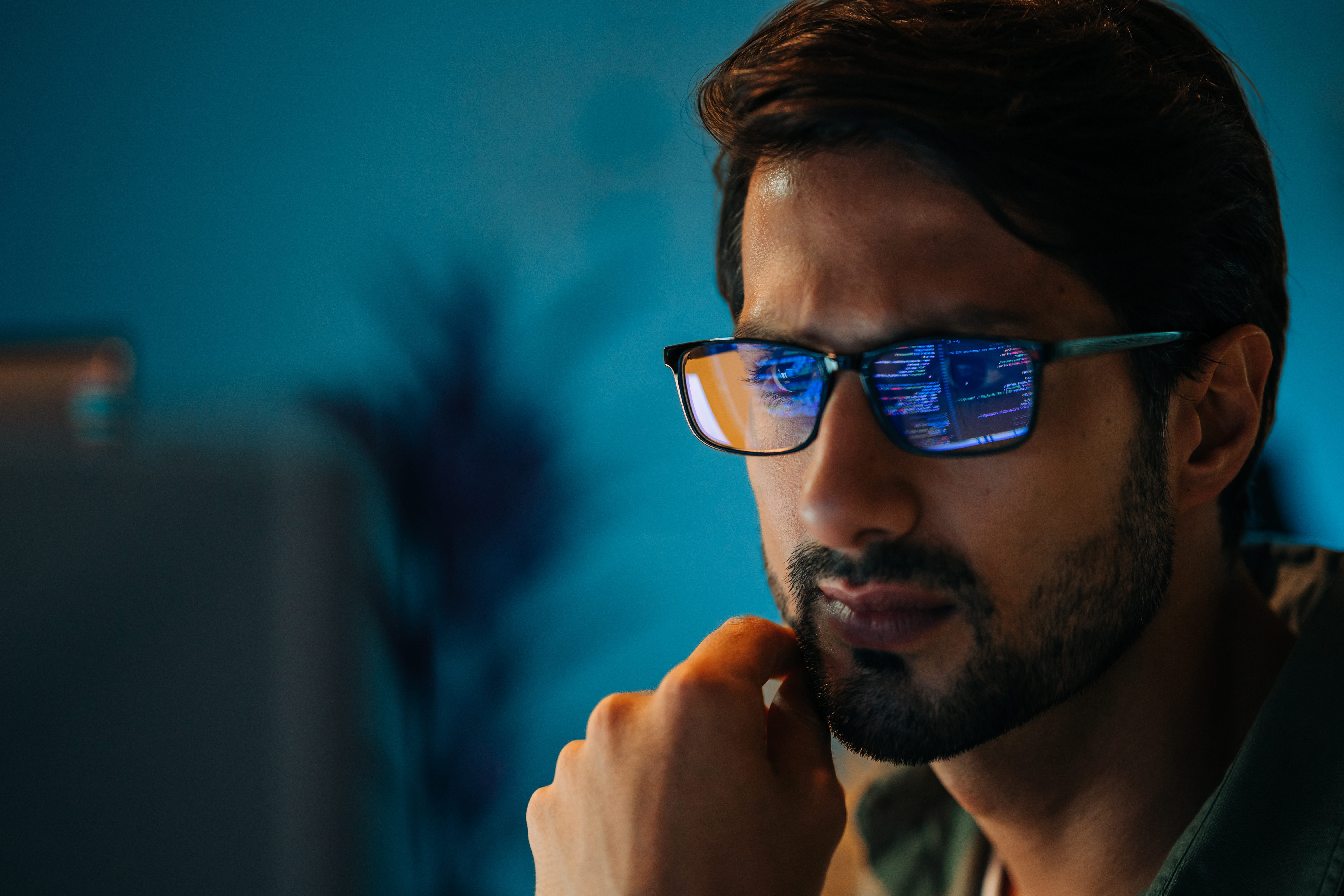 Male AI practitioner with glasses reflecting lines of code, blue-tinted studio portrait